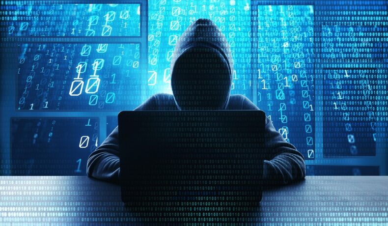 Hacker care încearcă să acceseze un laptop. Are o glugă și nu i se vede fața. Pe fundal sunt litere albastre. Unii utilizatori cred că Internetul „a murit” acum 5 ani
