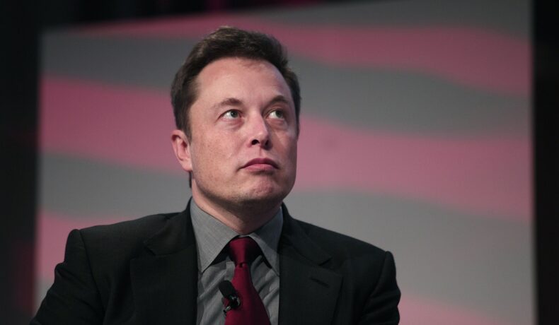 Elon Musk, la conferința Automotive News World Congress, în anul 2015. E pe scenă, îmbrăcat în costum negru, cămașă gri, cravată roșu cu negru. Elon Musk a dezvăluit opiniile sale despre natalitate