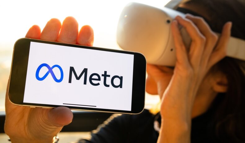Persoană care poartă o cască de realitate virtuală și are în mână un telefon, cu logo-ul Meta pe ecran, similar cu viziunea Meta pentru metavers