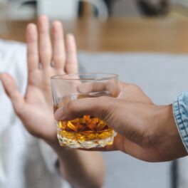 Persoană care are un pahar de alcool în mână și i-l oferă altcuiva, care îl refuză. Consumul de alcool poate afecta creierul, potrivit experților