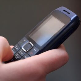 Mâna unui utilizator care ține un telefon simplu, negru, similar cu telefoanele „proaste” care au revenit în tendințe