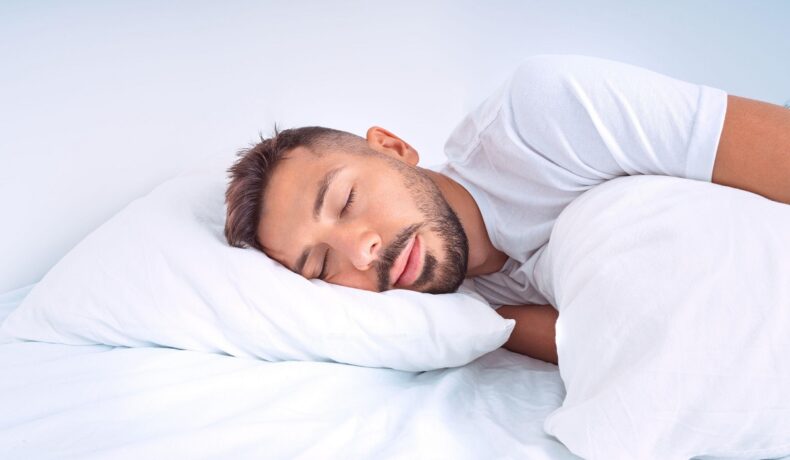 Bărbat care doarme într-un pat cu cearșafuri albe. Experții au dezvăluit recent câte ore trebuie să dormi pe noapte