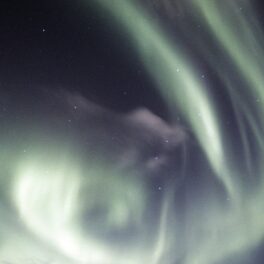 Aurora boreală pe cer, cu nuanțe de alb, pe fundal întunecat. Recent, o „meduză spațială” a fost surprinsă pe cer