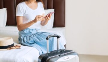 Femeie care stă pe pat, lângă bagaje, în camera de hotel. Experții au dezvăluit cum îți poți proteja lucrurile din camera de hotel