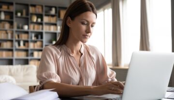 Femeie care scrie la un laptop alb, în timp ce stă la birou. O altă femeie câștigă 1 milion de dolari pe an prin trimiterea de email-uri