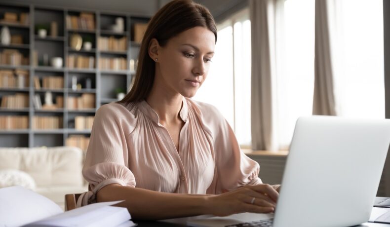 Femeie care scrie la un laptop alb, în timp ce stă la birou. O altă femeie câștigă 1 milion de dolari pe an prin trimiterea de email-uri