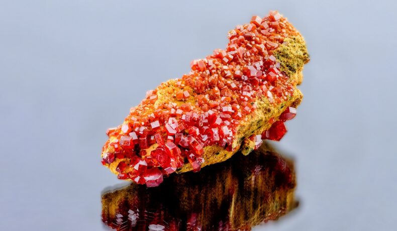 Mineral de vanadinit, roșu și portocaliu, pe fundal gri. Oxidul de vanadinit e compusul care are memorie