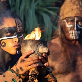 Mayași care participă la o ceremonie, unul dintre ei are simboluri pe față și ține o cupă cu foc în mâini. Sacrificiile umane din „Peștera Terorii” au uimit experții