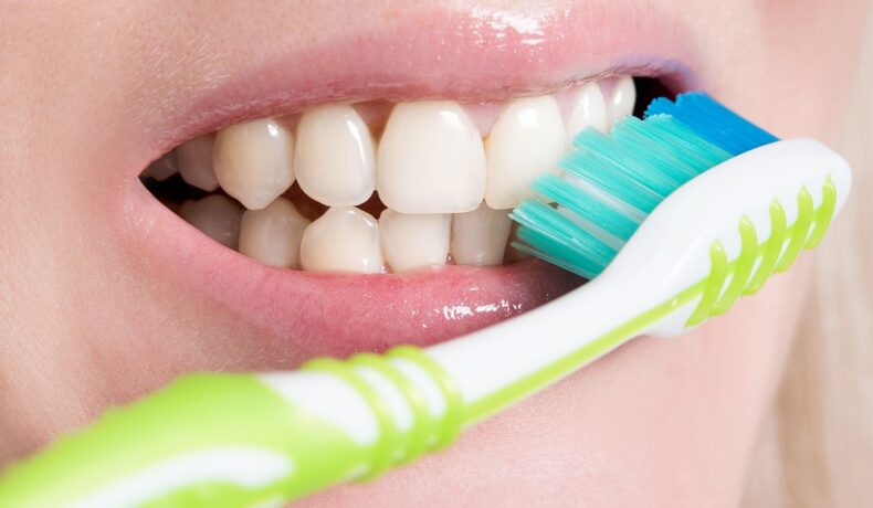 Copil care se spală pe dinți cu o periuță cu alb și verde. Experții susțin că organismele care pot „umbla” pe dinții oamenilor produc carii