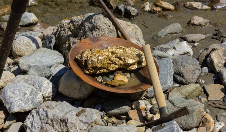 Rocă de aur într-o farfurie din metal, cu un târnăcop, printre pietre, pentru a ilustra cum un bărbat a găsit 2 roci imense