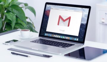 Laptop deschis pe o masă albă, cu o plantă în stânga, cu Gmail pe ecran, pentru a ilustra emailul „neobișnuit” care îți poate goli contul bancar