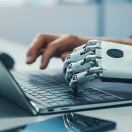 Persoană cu o mână umană și o mână albă de robot, care scrie pe tastatura unui laptop, pentru a ilustra schimbarea care ar putea fi „mai profundă” decât focul