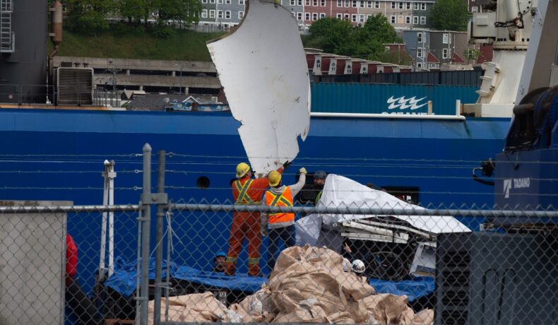 Muncitori care ajută să direcționeze resturile submersibilului Titan, aduse recent la suprafață, fotografiați după un gard, iunie 2023, Canada