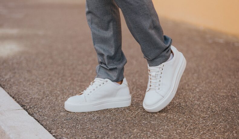 Bărbat care poartă o pereche de pantofi sport albi, cu pantaloni gri, care merge pe stradă, similară cu o pereche de pantofi sport Apple