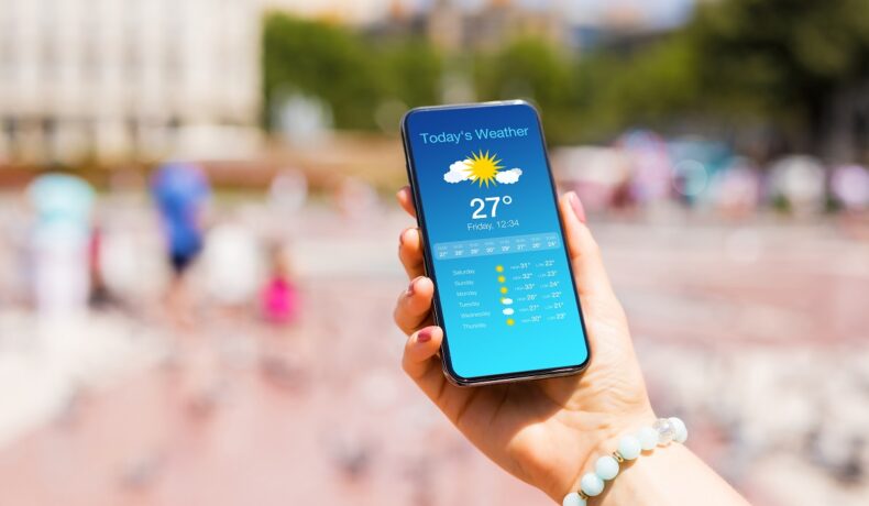 Utilizatoare care ține în mână un telefon pe care apare o aplicație meteo care spune că sunt „30% șanse de ploaie”