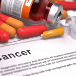 Pastile în nuanțe de roșu și portocaliu, pe o hârtie albă pe care scrie cancer, similară cu „pastila care ucide cancerul”