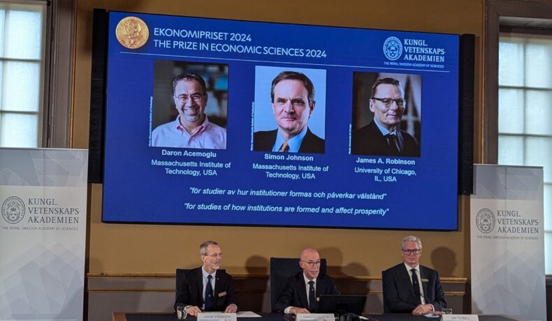 Anunțarea câștigătorilor Daron Acemoglu, Simon Jonhson şi James Robinson pentru Premiul Nobel Pentru Economie în 2024, pe ecran albastru în spatele economiei