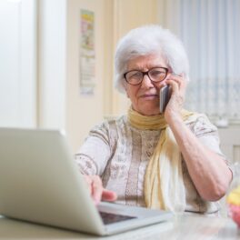 Bunicuță care vorbește la telefon în timp ce se uită la un laptop, ca bunicuța AI