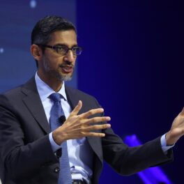 Sundar Pichai, CEO-ul Google care apără inteligența artificială, îmbrăcat în costum, pe fundal albastru